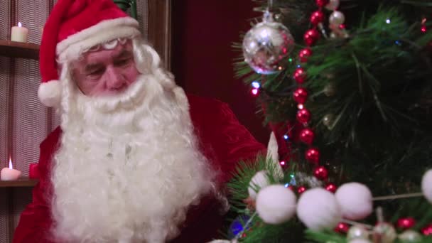 Modern Santa Claus looks at the branches with balls in close-up and admires him. — Stock Video