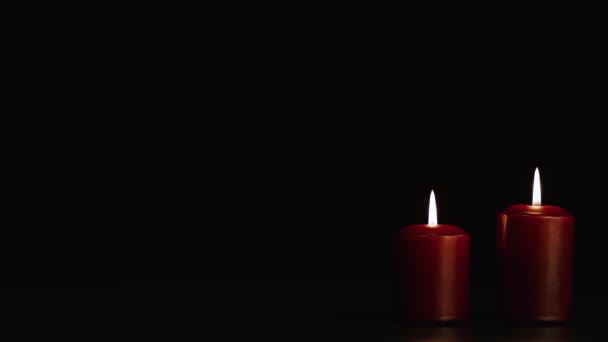 Dos velas rojas misteriosamente encendidas sobre un fondo negro. Copiar espacio. — Vídeo de stock