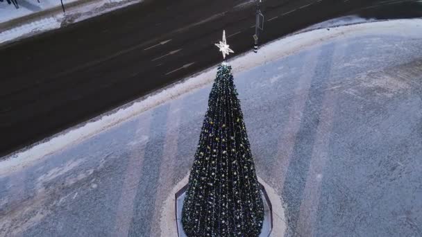 Un esbelto árbol de Navidad con guirnaldas brillantes en la plaza de la ciudad, vista aérea. — Vídeo de stock