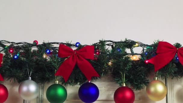 Kerstmis kleurrijke ballen hangen op een bloemenslinger van een groene tak. — Stockvideo