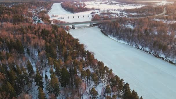 Un majestuoso paisaje invernal con un río congelado y un puente al atardecer, aéreo — Vídeos de Stock