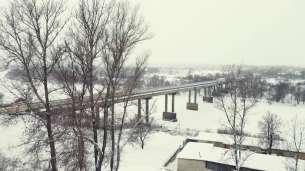 Sněžná zimní krajina se zamrzlou řekou a silničním mostem, letecký pohled. — Stock video