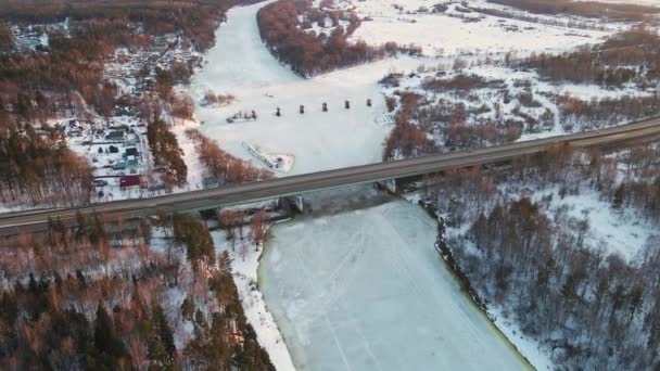Perfektní zimní krajina se zamrzlou řekou a mostem při západu slunce, letecký pohled. — Stock video