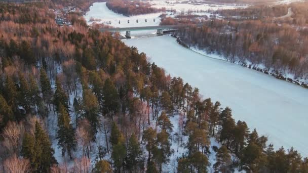 Ruhige Winterlandschaft mit gefrorenem Fluss und Brücke bei Sonnenuntergang, Luftaufnahme. — Stockvideo
