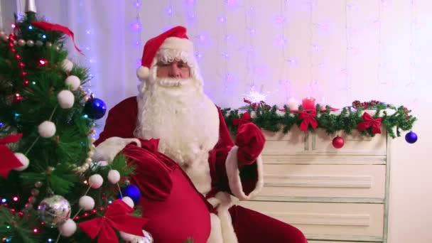 Der moderne Weihnachtsmann hält einen Sack voller Geschenke in der Hand und winkt mit einer brennenden Wunderkerze. — Stockvideo
