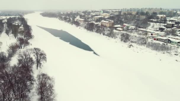 Снежный зимний пейзаж с замерзшей рекой и пригородами, вид с воздуха. — стоковое видео