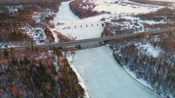Романтичний зимовий пейзаж з замерзлою річкою і мостом на заході сонця, вид з повітря . — стокове відео