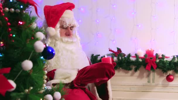Modern jultomten tittar på ett brinnande rött ljus i närbild. — Stockvideo