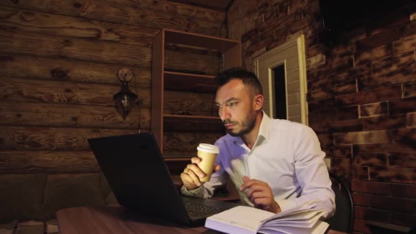 Um homem de negócios está bebendo café, olhando para a tela e em um caderno. — Vídeo de Stock