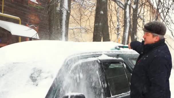 Ένας άνθρωπος καθαρίζει ένα σώμα αυτοκινήτου από το χιόνι με ένα πινέλο. — Αρχείο Βίντεο