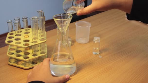 Pupils hands close-up pouring a chemical reagent from a glass into a flask. — 图库视频影像