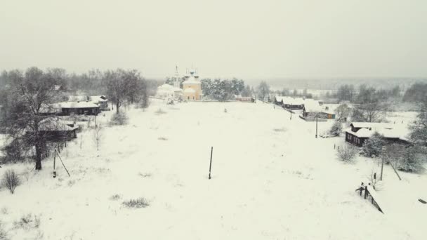 Зимний пейзаж заснеженной деревни с деревянными домами и церковью, вид с воздуха. — стоковое видео