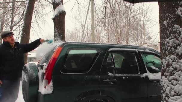 Un hombre limpia la nieve del techo de un coche con un cepillo. — Vídeo de stock