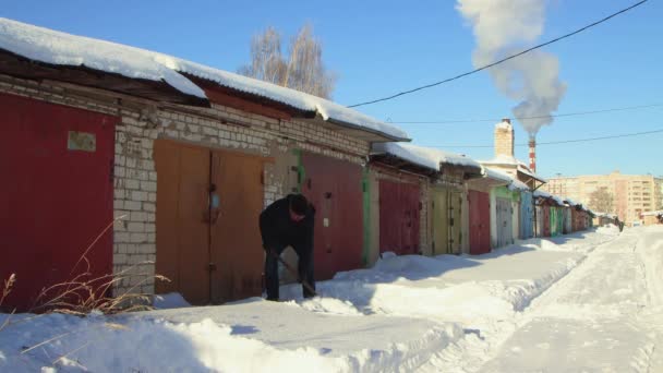 Um homem com uma pá limpa cuidadosamente a neve da estrada fora de sua garagem. — Vídeo de Stock