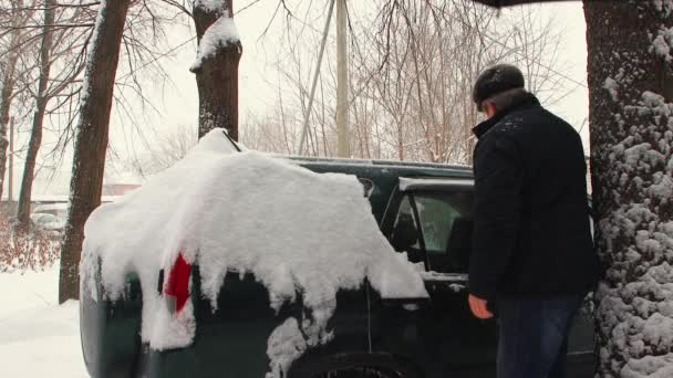 Un hombre limpia la nieve de una carrocería con un cepillo. — Vídeo de stock