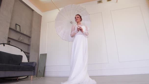Beautiful bride in a white dress poses for the photographer with an umbrella. — Stock Video
