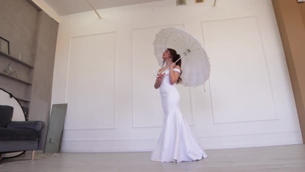 Sposa timida in un abito bianco in posa mentre in piedi con un ombrello. — Video Stock