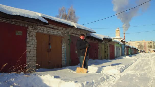 Un hombre con ropa de abrigo se apoya en una pala de madera, limpiando la nieve. — Vídeos de Stock