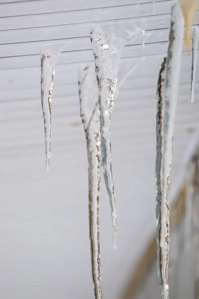 Frozen ice icicles hang under the plastic visor of the roof edge. — Stock Photo, Image