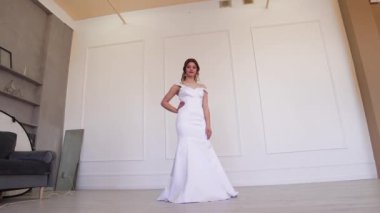 Beyaz elbiseli mutlu gelin ayakta dururken fotoğrafçıya poz veriyor..