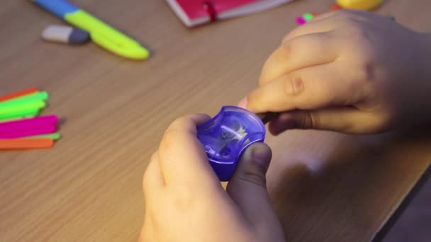 Close-up student hands sharpen a pencil in a blue sharpener. — Stock Video