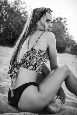 Siyah külotlu ve tişörtlü güzel bir esmer manken. Kumların üzerinde, kameranın önünde poz vermek. Yakın çekim ve uzun menzilli çekim.