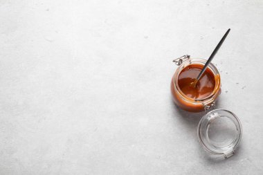 Gri arka planda cam kavanozda ev yapımı tuzlu karamel sosu. Boşluğu kopyala, üst görünüm.