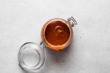 Gri arka planda cam kavanozda ev yapımı tuzlu karamel sosu. Boşluğu kopyala, üst görünüm.