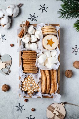 Lezzetli ev yapımı kurabiyeler, marşmelovlar ve gri arka planda krema içeren bir hediye kutusu. Noel ve Yeni Yıl konsepti. Zencefilli çörek, Avustralya linzer kurabiyesi, bisküvi. Üst manzara, tatil düzlüğü.