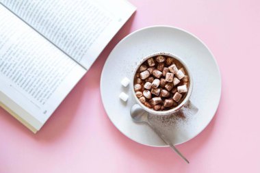 Seramik bardakta kremalı sıcak kakao ve pembe arka planda kitap. Kış ya da sonbahar konsepti. En düşük tasarım.