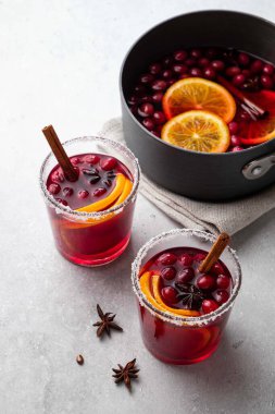Noel için sıcak şarap, kızılcık, baharat, tarçın ve portakal dilimleri ile beyaz masada iki cam bardak ve tencere. Seçici odak.
