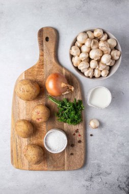 Gri masadaki mantar kremalı çorba için gerekli malzemeler. Şampiyon, krema, patates, soğan, maydanoz, ahşap tahtada tuz ve baharat. Üst görünüm.