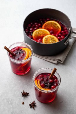 Noel için sıcak şarap, kızılcık, baharat, tarçın ve portakal dilimleri ile beyaz masada iki cam bardak ve tencere. Seçici odak.
