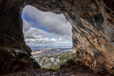 İçeriden Bolumini mağarası, arka planda mavi gökyüzü ile karlı bir manzara. Mariola Doğal Parkı, Katılıyorum, Alicante, İspanya.