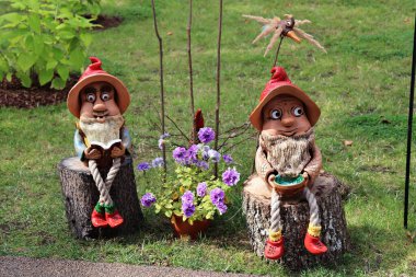 Fabulous funny gnomes made of burnt clay sitting on wooden stumps.