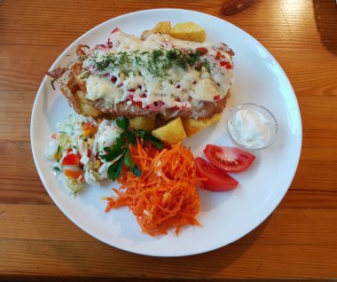 Pork chop with cheese fried potatoes and fresh vegetable salad on a white plate.