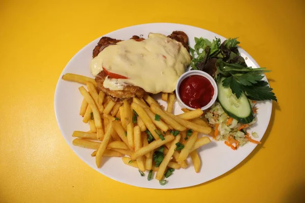Pork chop with cheese fried potatoes and fresh vegetable salad on a white plate.