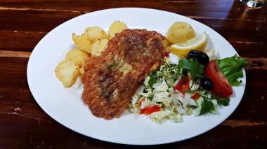 Bir parça kızarmış balık ve haşlanmış patatesle beyaz tabakta taze salata..