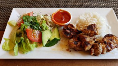 Ateşin üstünde kızarmış domuz parçaları ve beyaz tabakta taze sebze salatası..