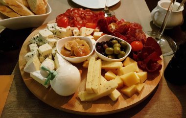 Çeşitli peynir ve sosis türleri zeytin, mantar ve domatesler ahşap bir tepside dilimlenir..