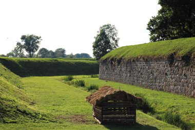 Kale duvarının önünde yeşil otlarla kaplanmış büyük bir çukur var..