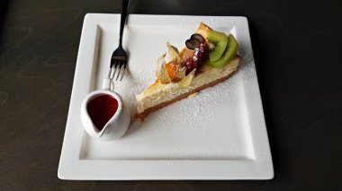 Büyük bir dilim pasta ve beyaz bir tabakta vişne reçelli sos kabı..