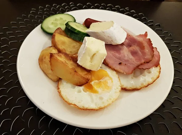 Жареные яйца с беконом и ломтики сыра на белой тарелке на завтрак — стоковое фото