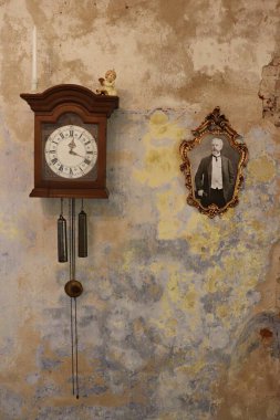 Ağırlıkları olan antika bir saat ve duvarda bir adamın çok eski bir çerçeveli fotoğrafı..
