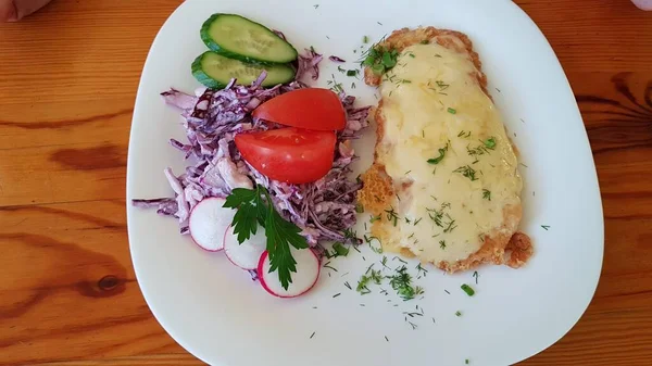 Peynirli kızarmış domuz eti ve beyaz tabakta taze sebze salatası..