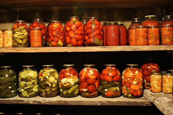 Домашние овощи, консервированные в стеклянных банках, выставлены на полках в подвале.