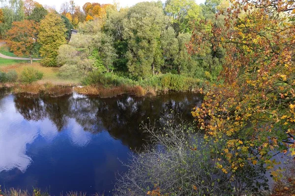 Pequeño lago con nubes blancas reflejadas y árboles con hojas coloridas de otoño — Foto de Stock