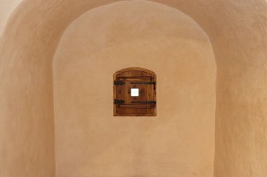 Bej renklerle boyanmış bir duvardaki ahşap panjurun kapattığı küçük pencere..