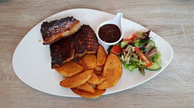 Büyük beyaz tabakta ızgara domuz eti ve patates..