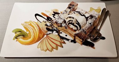 Elma dilimleri, portakal ve kivi ile beyaz tabakta lezzetli meyveli turta..